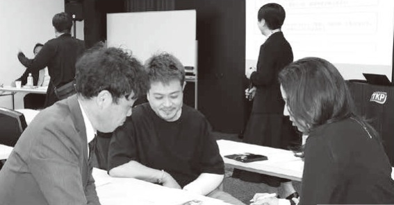 令和7年度「経営者研修」の会場風景と講師の中島尚美氏・高垣小売振興委員長、ペアワーク／グループワークに取り組む受講者